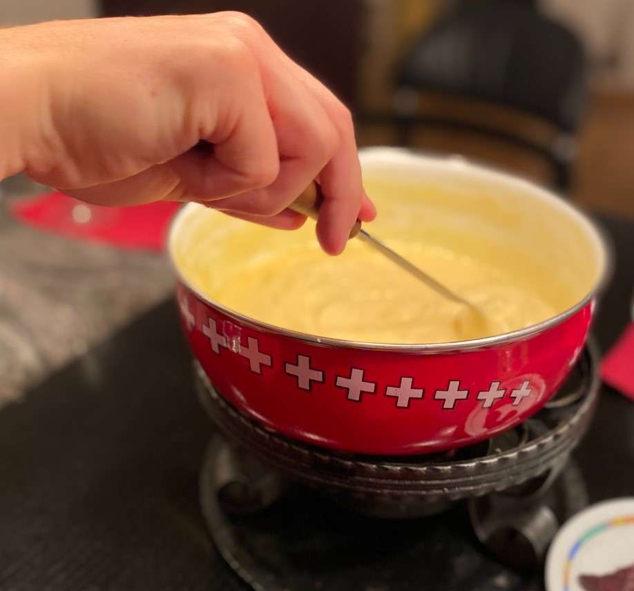 A woman's hand dips a piece of food into a pot of melted cheese.