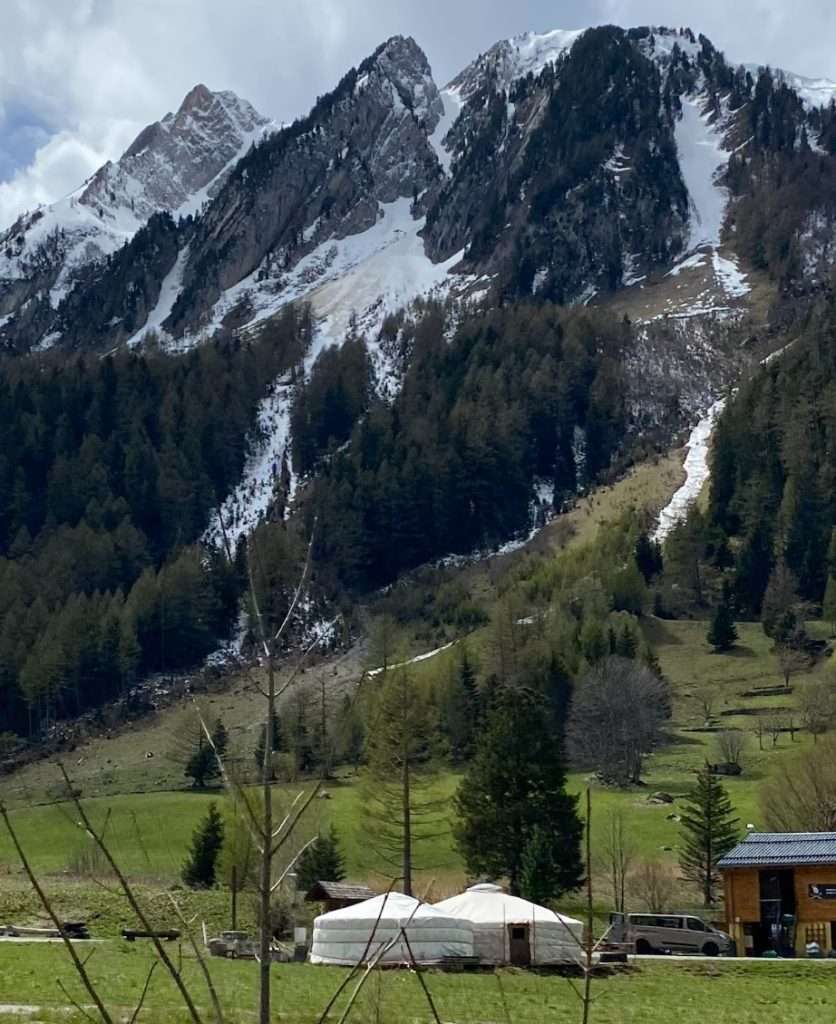 A white yurt with rugged, snow-covered mountains behind it.